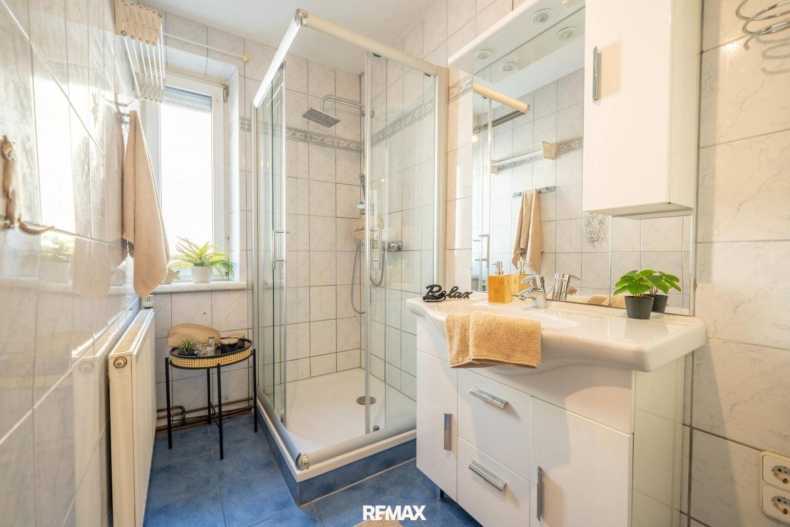 Badezimmer mit Duschkabine, Waschbecken und Fenster für Tageslicht.