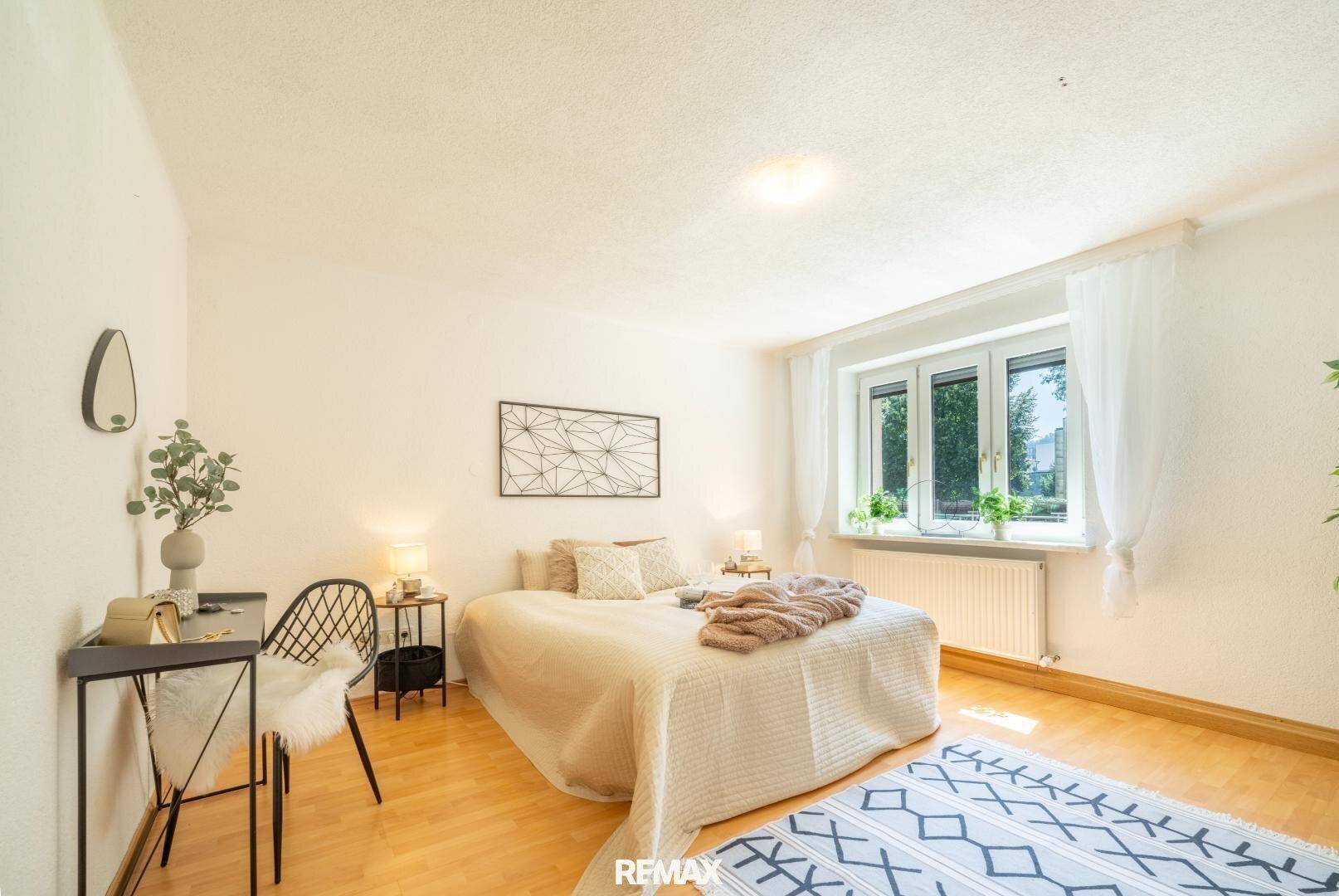 Helles Schlafzimmer mit Doppelbett, Parkettboden und Blick ins Grüne.