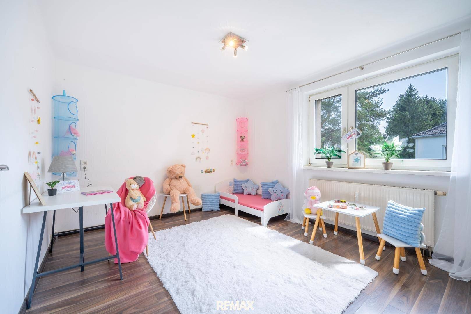 Helles Kinderzimmer mit Spielbereich, kleinem Bett und großem Fenster für viel Tageslicht.