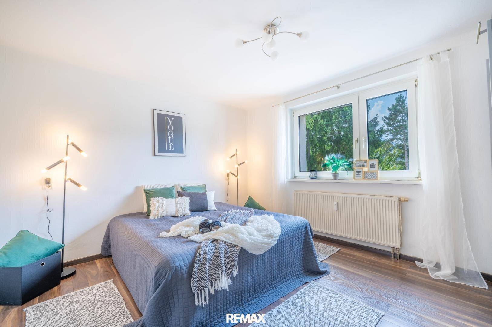 Helles Schlafzimmer mit großem Bett, modernen Stehlampen und Fenster mit Blick ins Grüne.