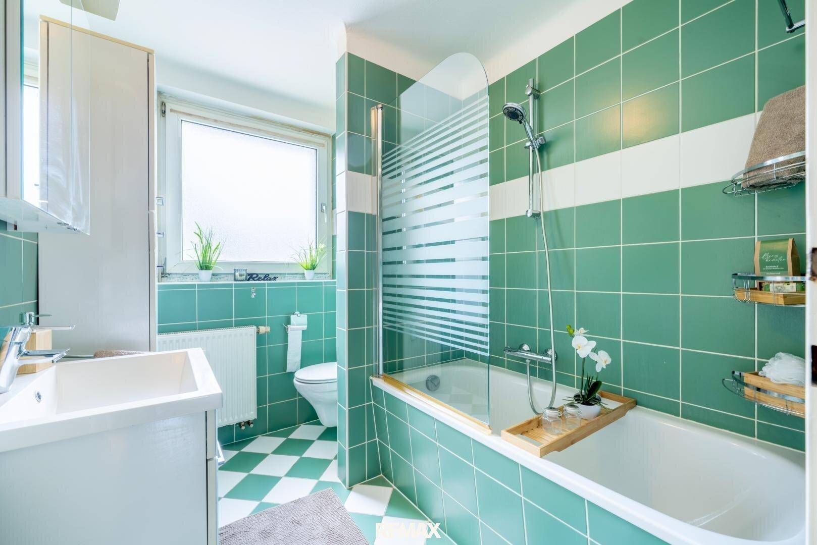 Badezimmer mit grünen Fliesen, Badewanne mit Duschfunktion und Fenster für Tageslicht.