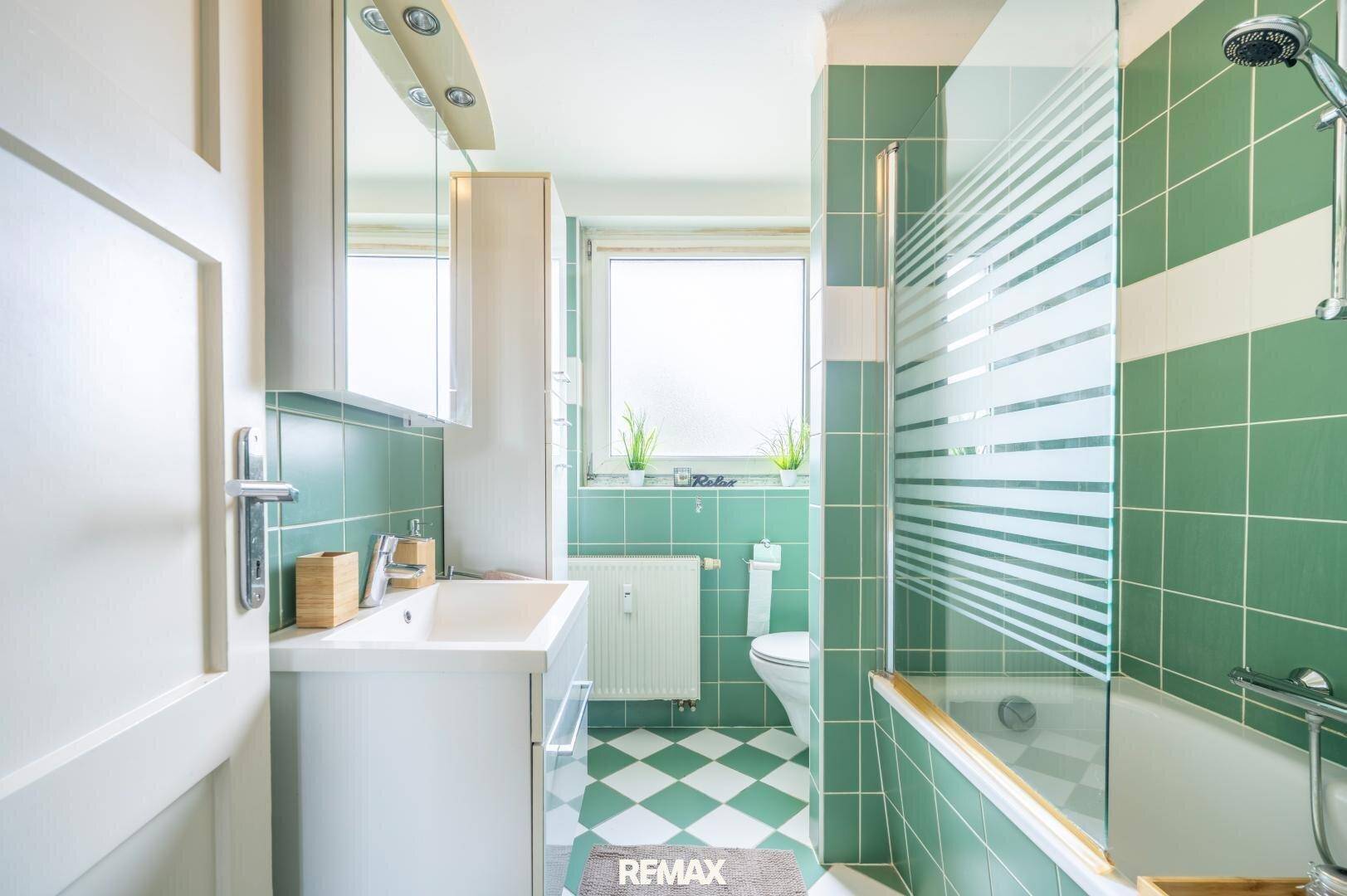 Funktionales Badezimmer mit grünen Wand- und Bodenfliesen, Waschtisch und Spiegelschrank.