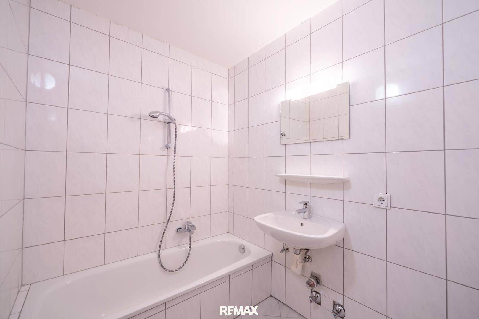 Gefliestes Badezimmer mit Badewanne, Duschfunktion und Waschbecken.