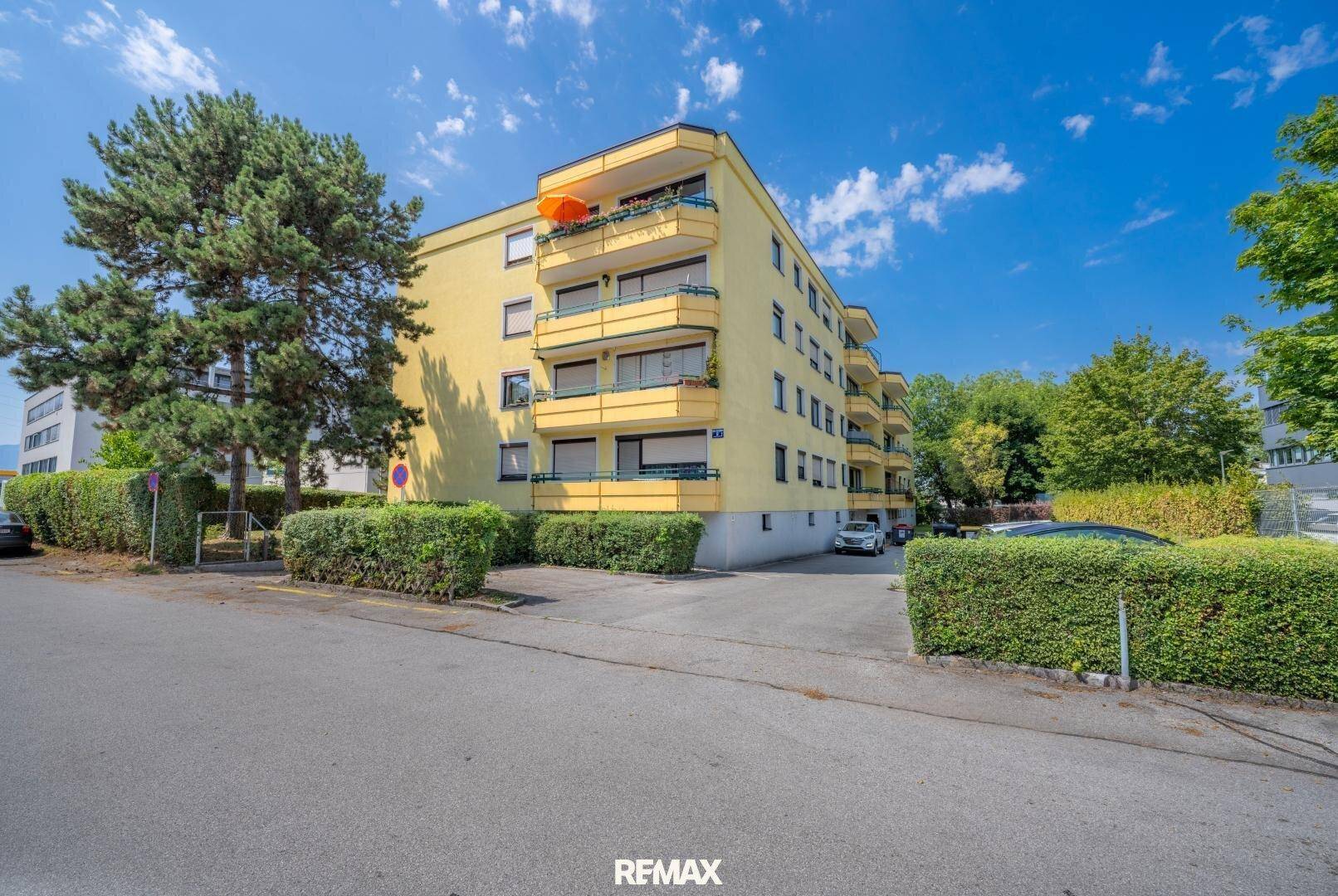 Mehrfamilienhaus mit gelber Fassade, Balkonen und umgebender Grünfläche.