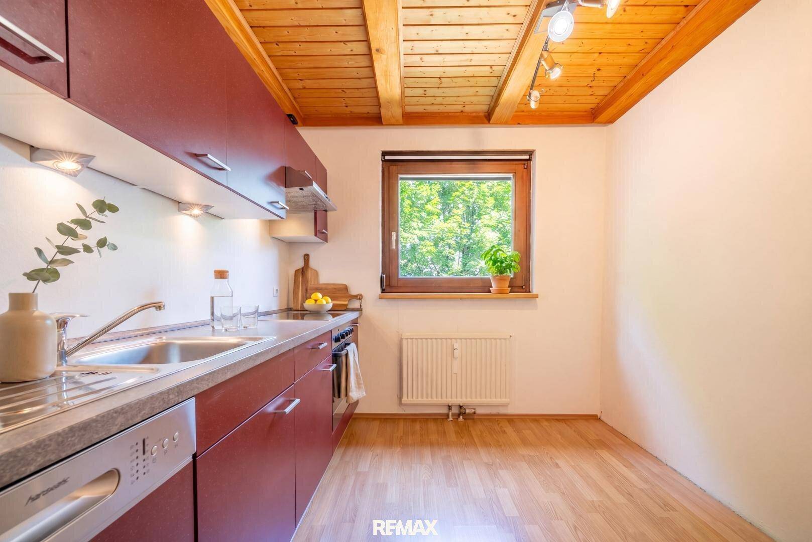 Virtuell inszenierte Küche mit roten Schränken, Holzbalkendecke und Fenster mit Blick ins Grüne.