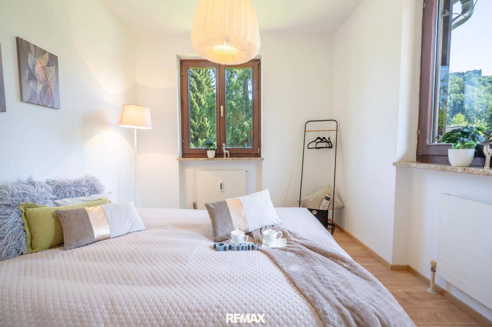 Helles Schlafzimmer mit großem Bett, Holzboden und Fenstern, die einen schönen Blick ins Grüne bieten.
