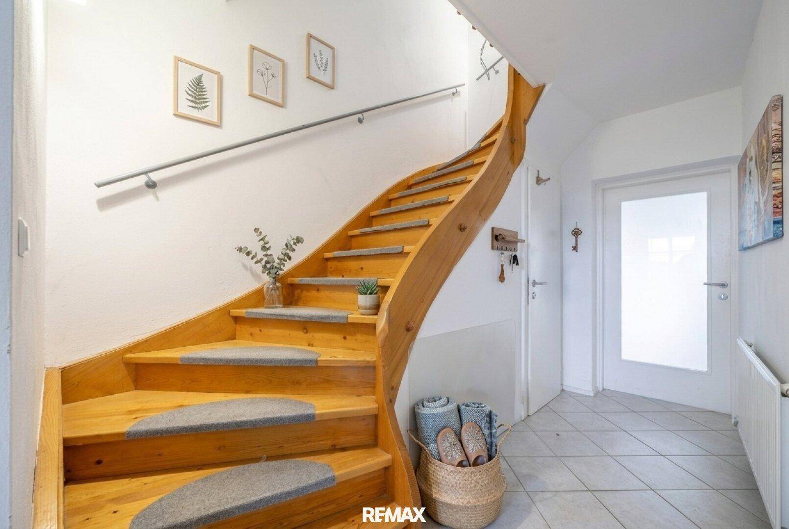 Heller Flur mit geschwungener Holztreppe und weiß gestrichenen Wänden, einladend gestaltet.