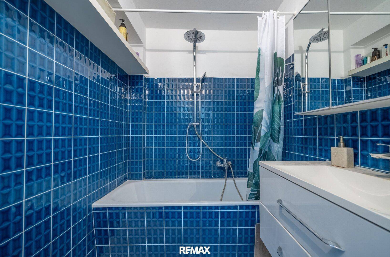 Badezimmer mit blauen Fliesen, Badewanne und integrierter Dusche, funktional eingerichtet.