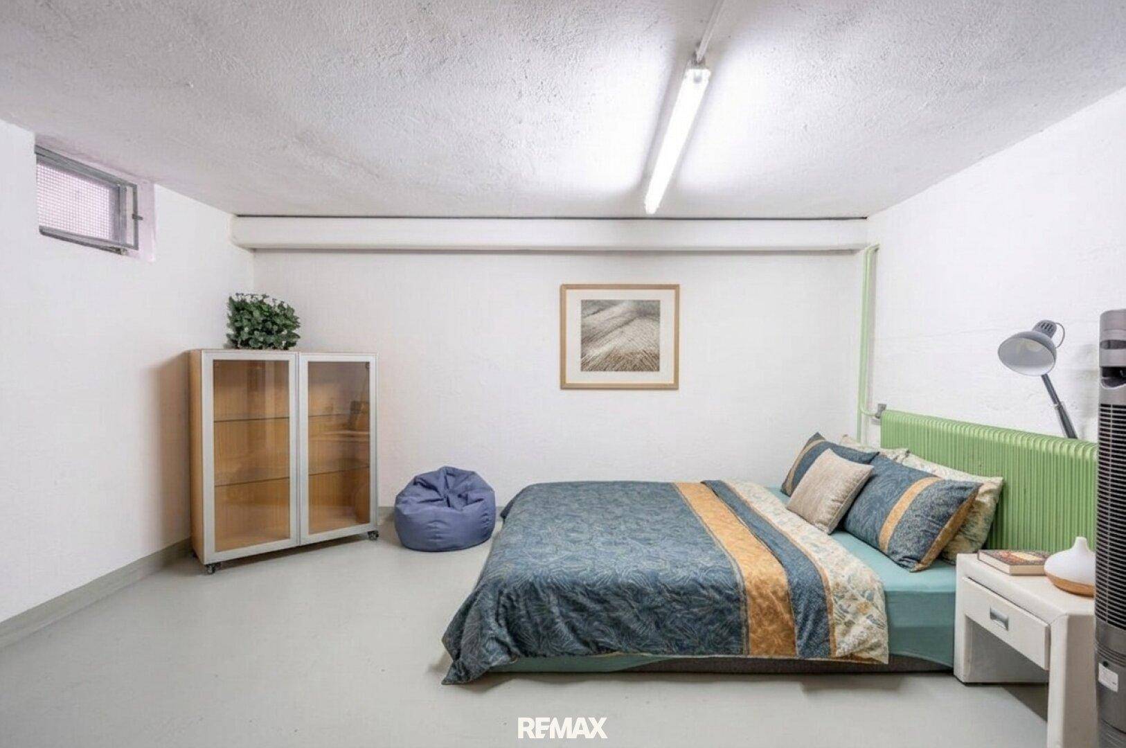 Ausgebauter Kellerraum, als Schlafzimmer genutzt, mit kleinem Fenster und einfacher Einrichtung.