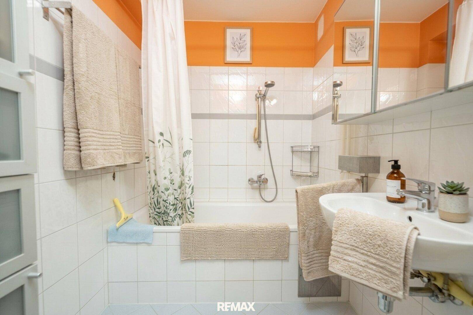 Funktionales Badezimmer mit Badewanne, Duschfunktion und weiß-orangefarbenen Fliesen.