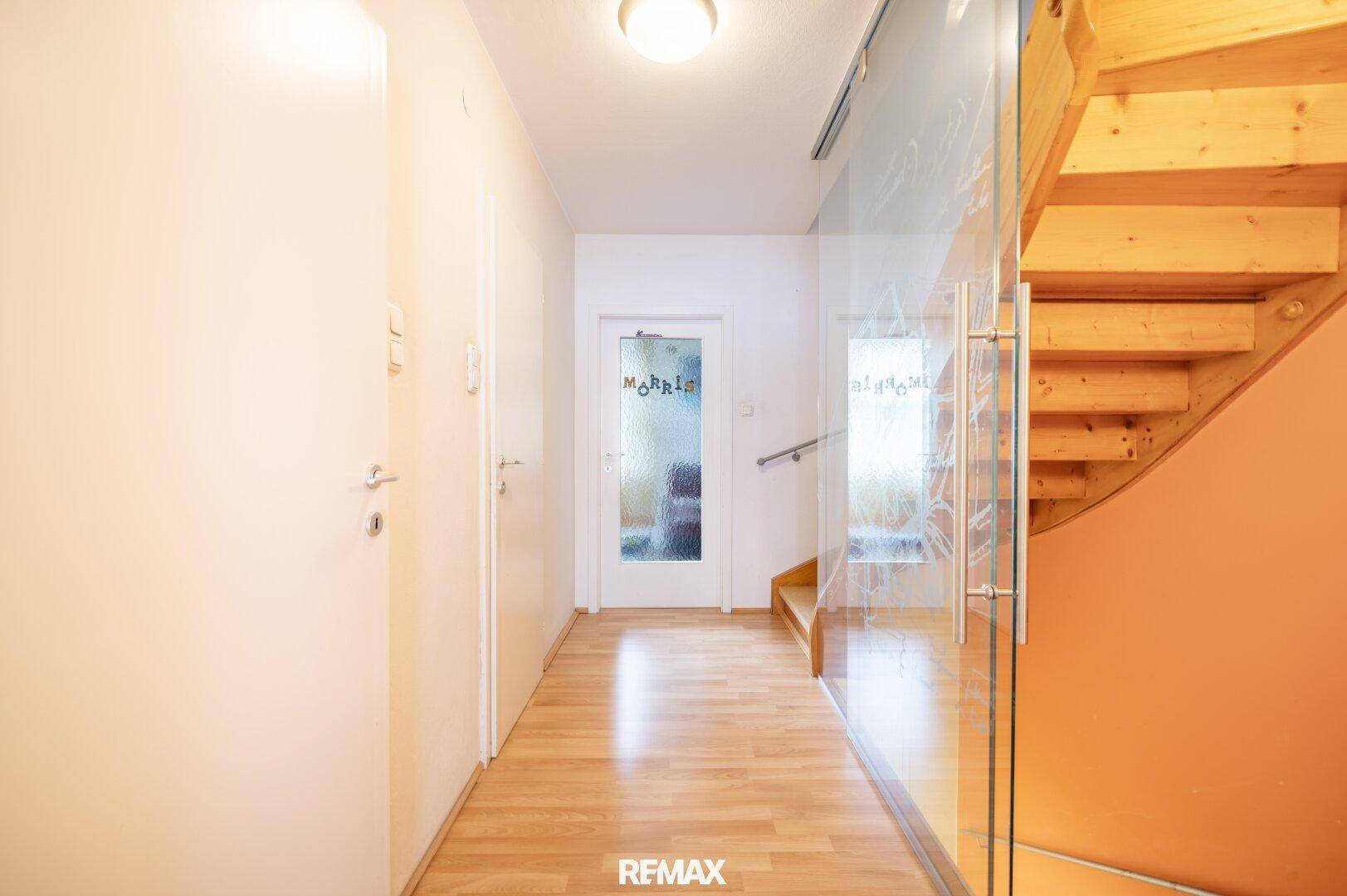 Heller Flur mit Holzboden, moderner Glaswand und Holztreppe.