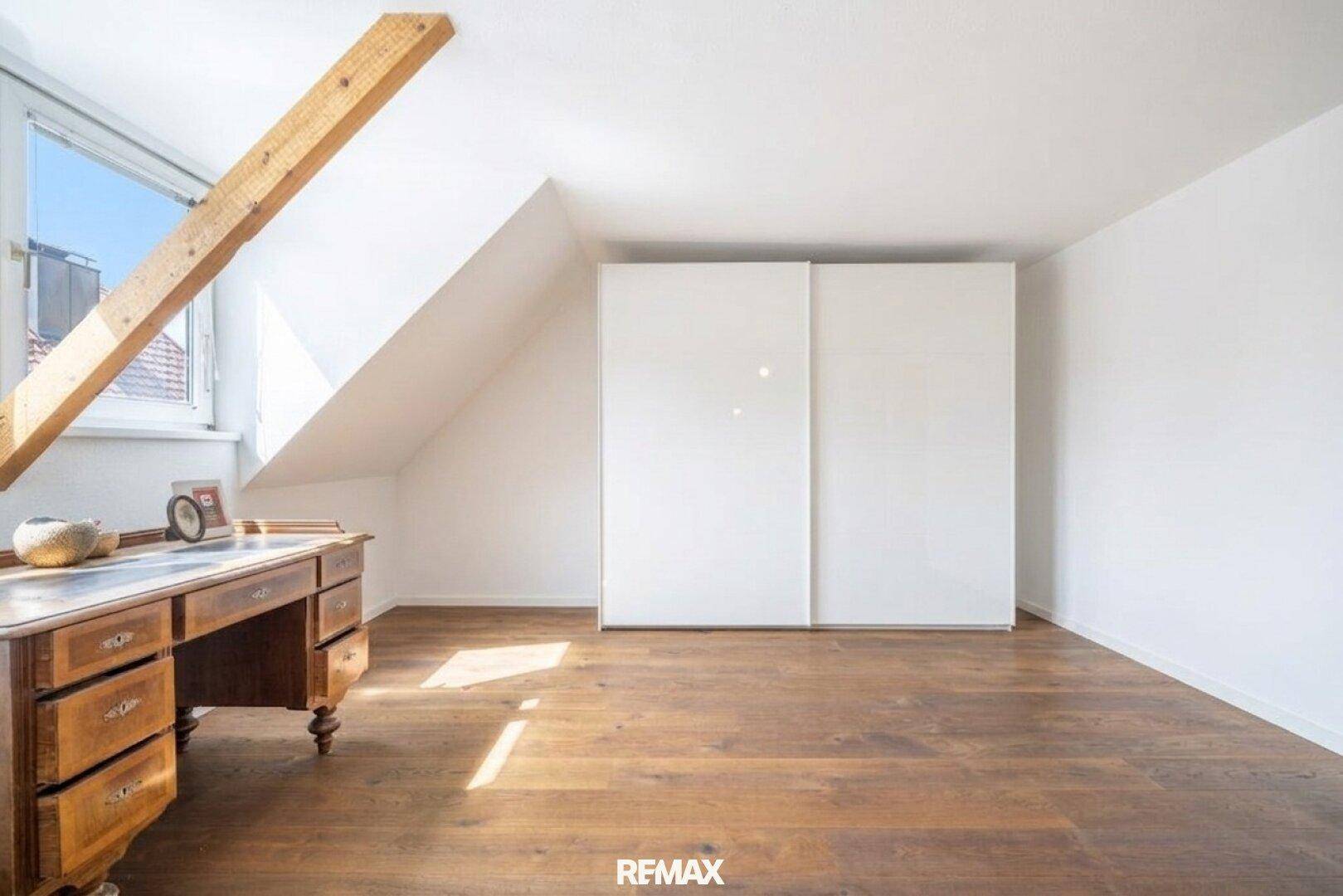 Dachgeschosszimmer mit Holzboden, Dachschräge und antikem Schreibtisch.