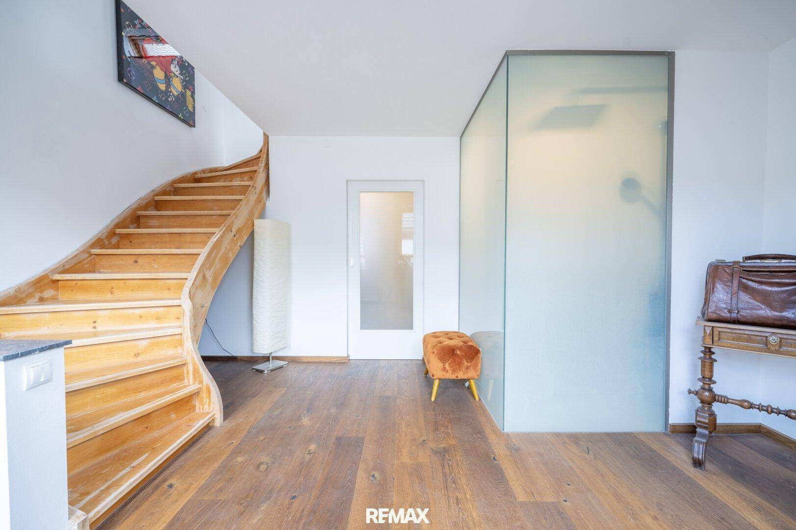 Heller Eingangsbereich mit Holztreppe und moderner Glasabtrennung.