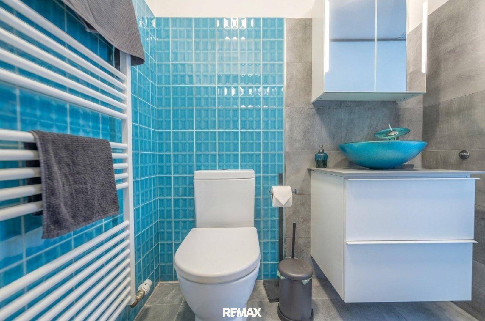 Modernes Badezimmer mit blauen Fliesen, wandhängendem WC und beheiztem Handtuchhalter.