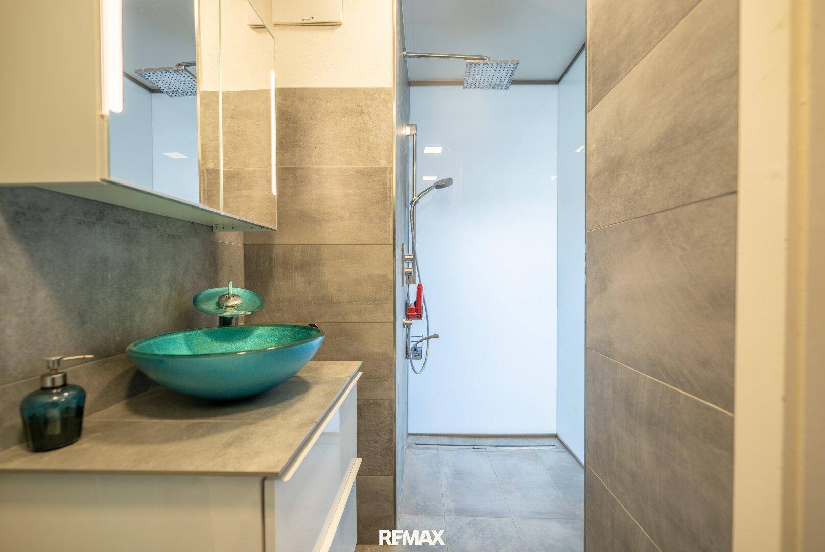 Modernes Badezimmer mit ebenerdiger Dusche, stilvollem Waschbecken und grauen Fliesen.