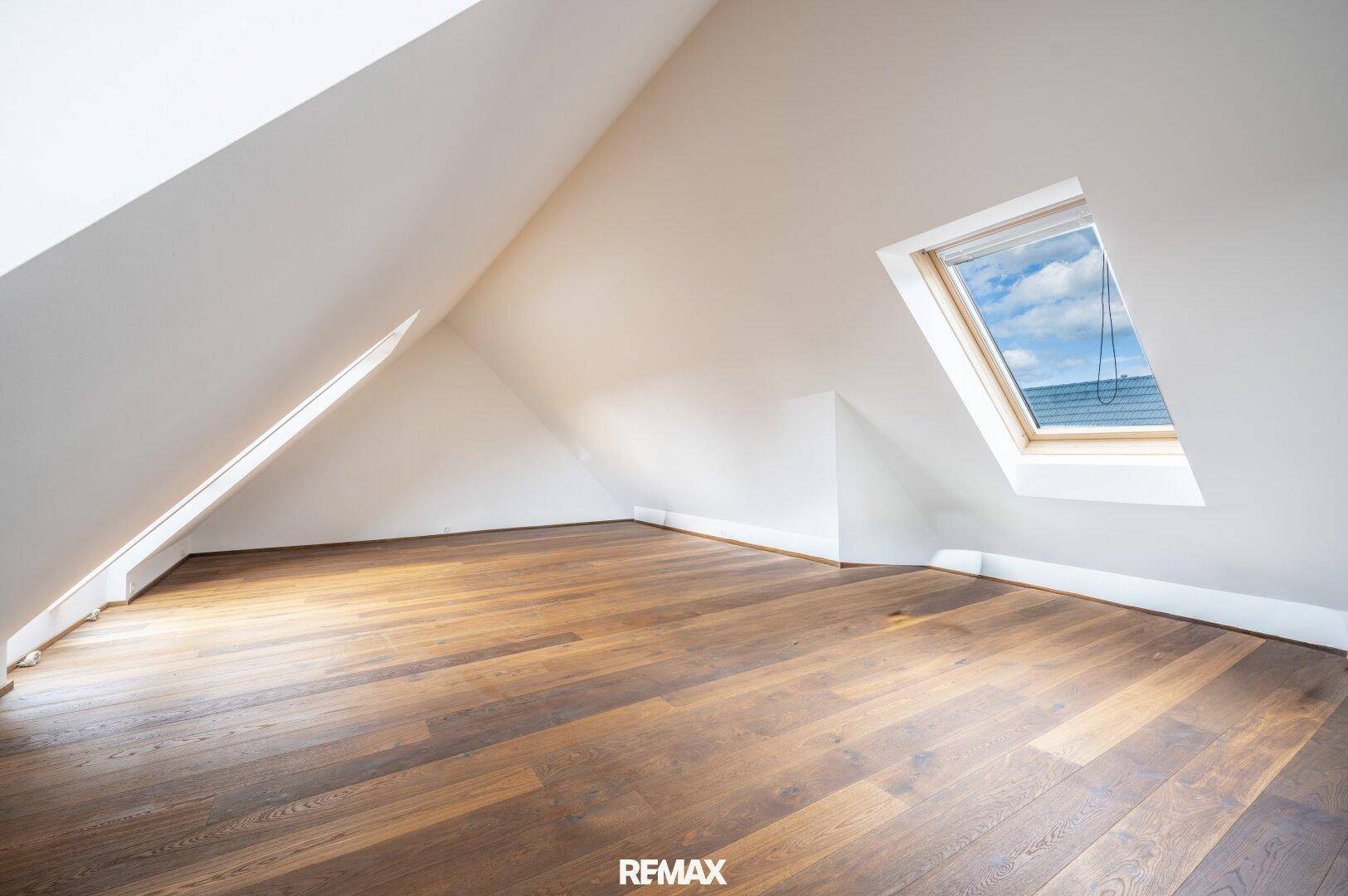 Geräumiges Dachgeschosszimmer mit Holzboden, Dachschräge und viel Tageslicht.