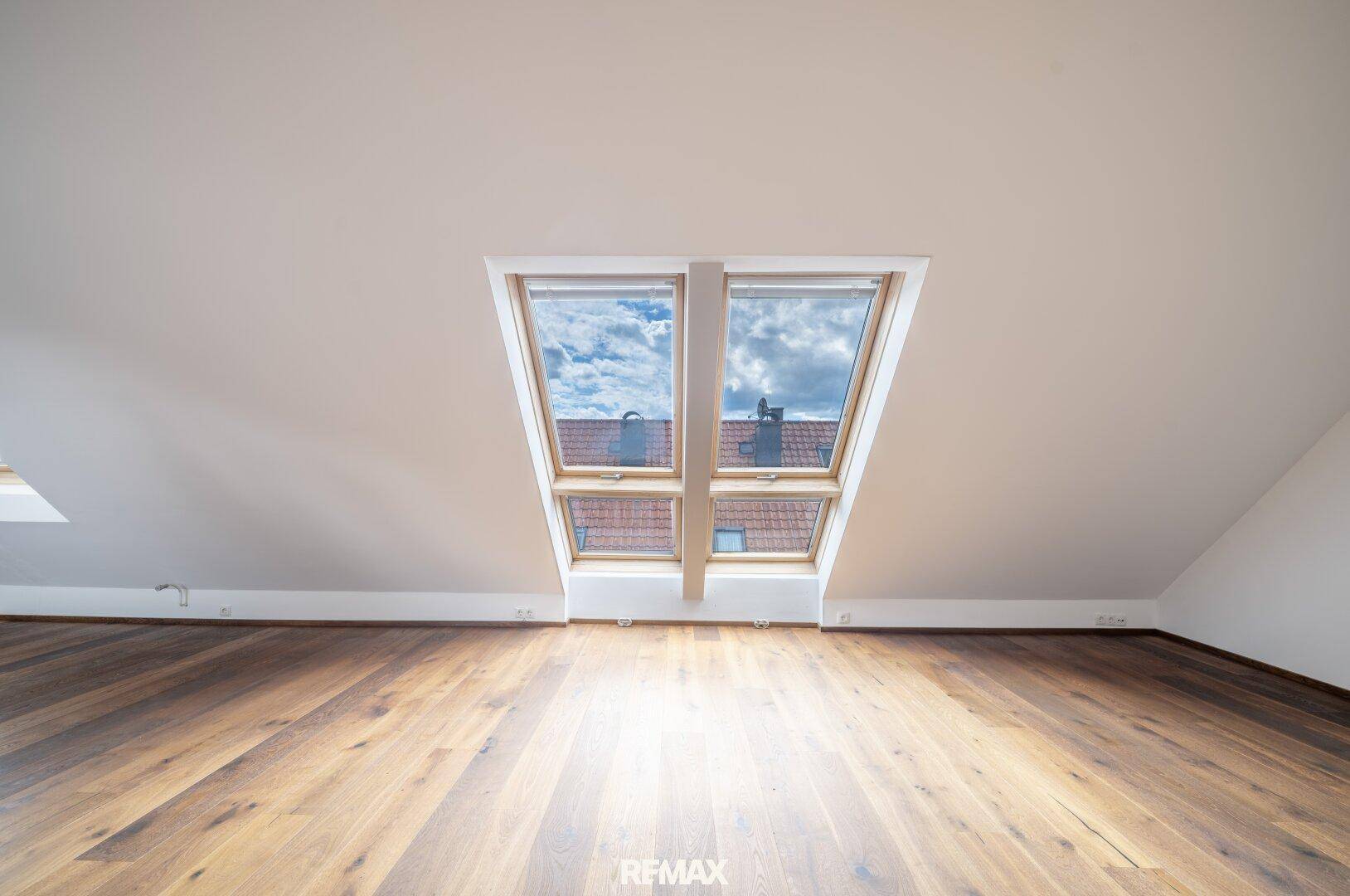 Helles Dachgeschosszimmer mit Holzboden, Dachschräge und zwei großen Dachfenstern.
