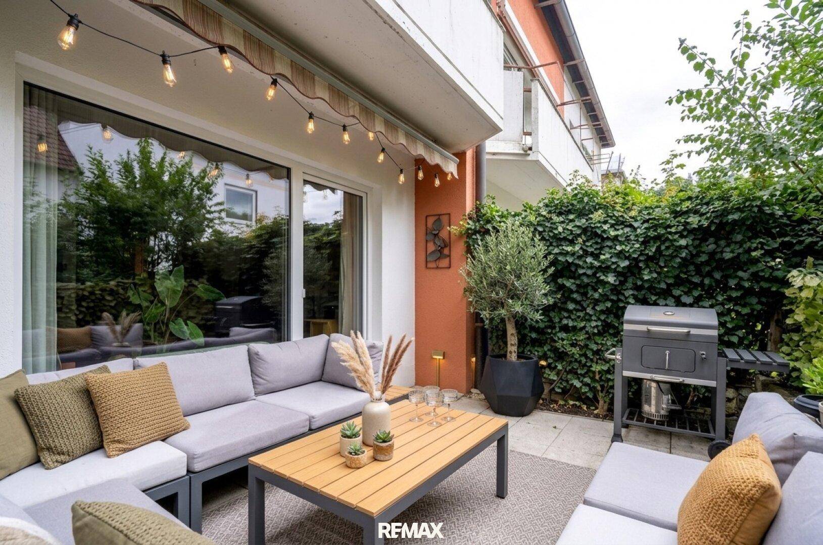 Einladende Terrasse mit Grillbereich und bequemer Lounge-Ecke, umgeben von grünen Pflanzen.