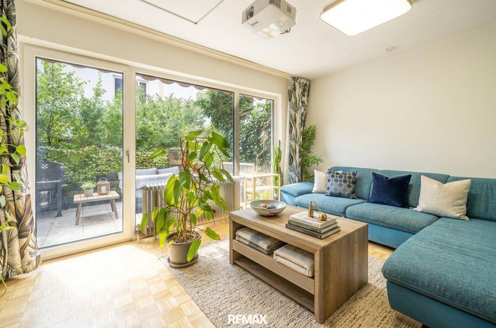 Helles Wohnzimmer mit großen Schiebetüren zur Terrasse und Blick ins Grüne, ausgestattet mit einem Projektor.