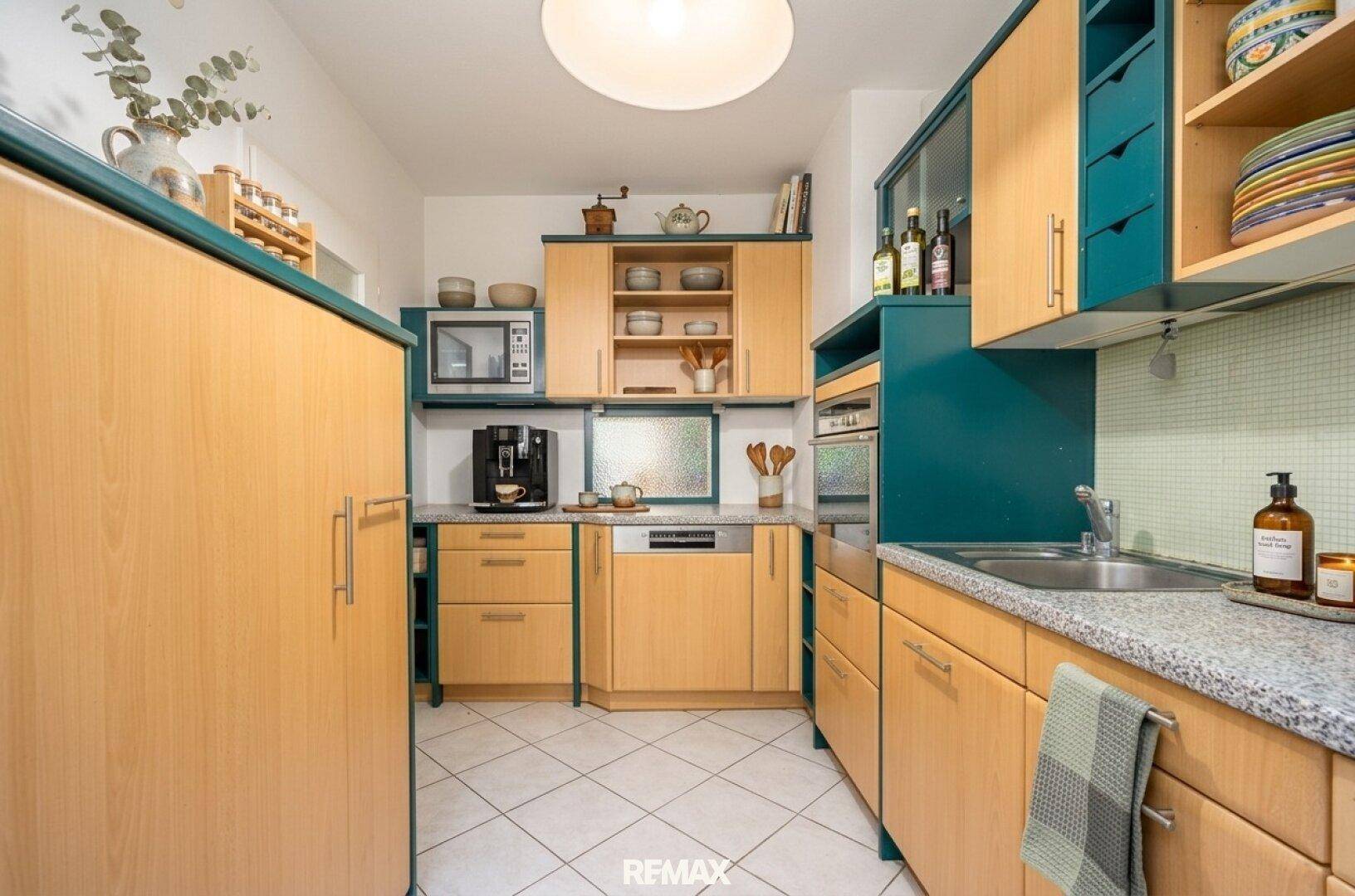 Voll ausgestattete Küche mit hellen Holzfronten, blauen Akzenten und modernen Geräten.