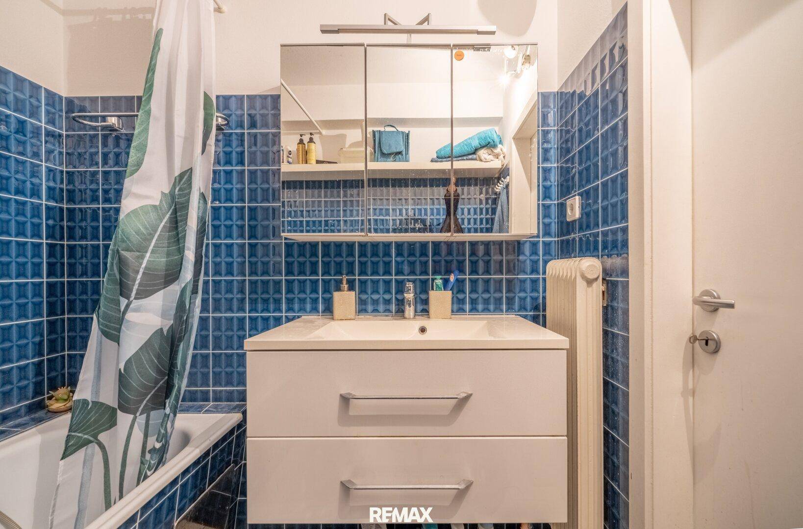 Badezimmer mit Waschbecken, Spiegelschrank und blauen Wandfliesen, gut beleuchtet.