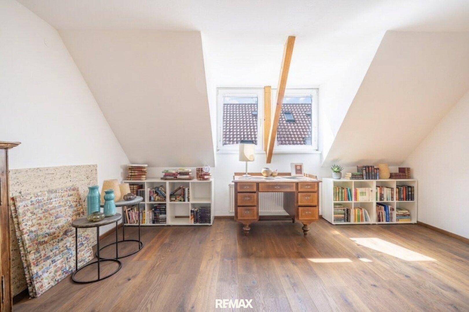 Helles Dachgeschosszimmer mit Holzboden, Dachschrägen und Bücherregalen.