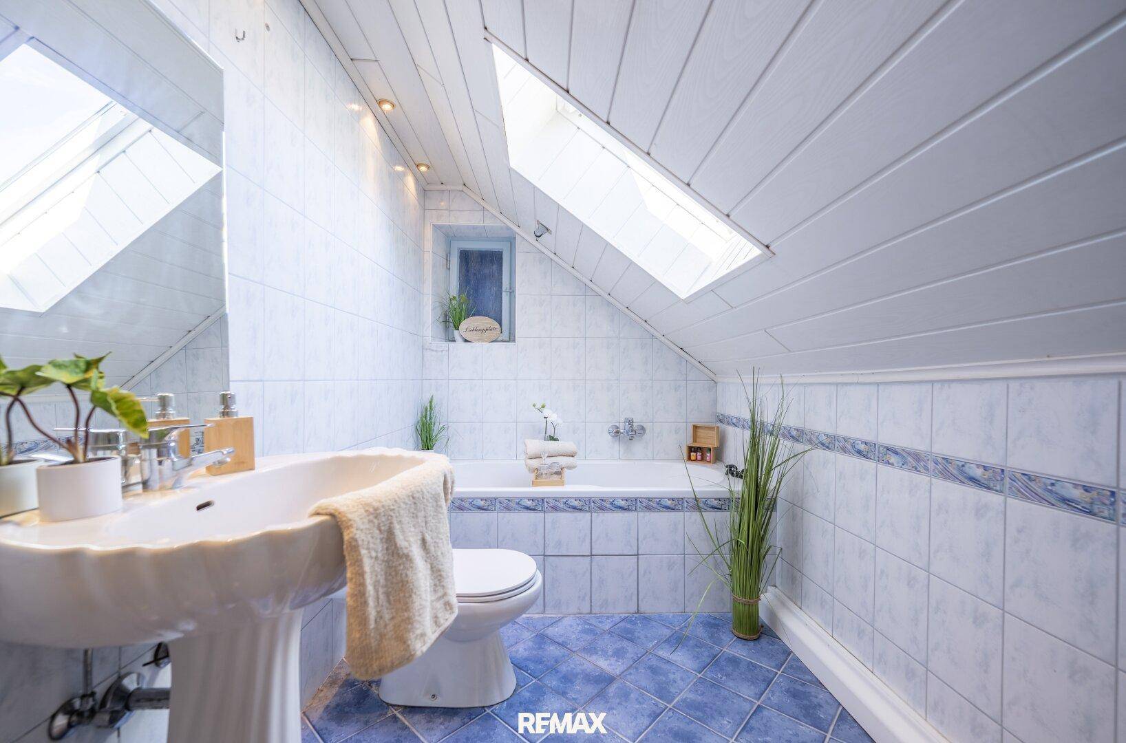 Badezimmer im Dachgeschoss mit schräger Decke, Dachfenster, Badewanne und blauen Fliesen.