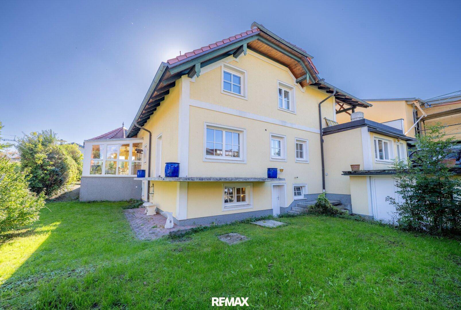 Rückseite des Hauses mit gepflegtem Rasen und einem hellen Wintergarten.