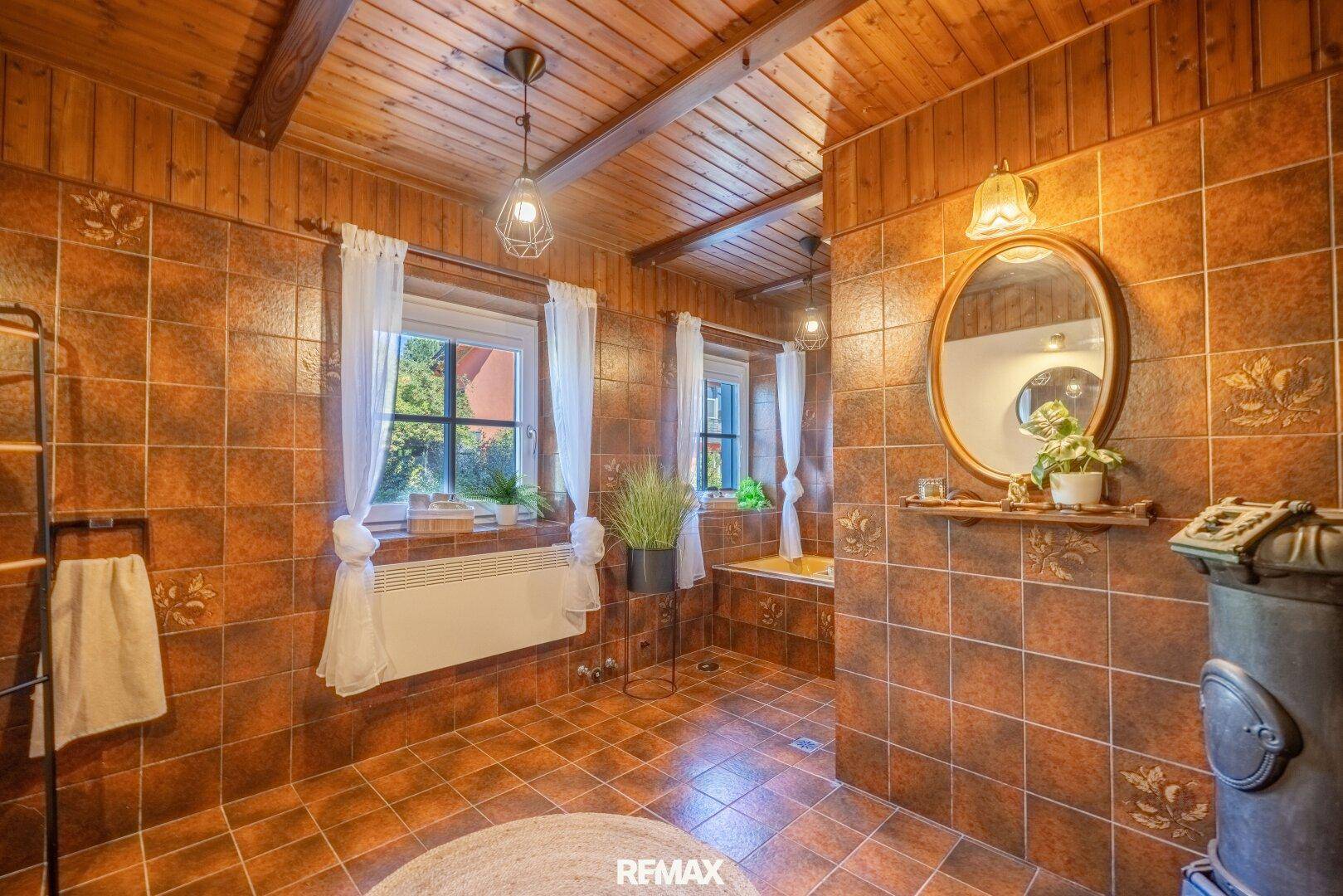Rustikales Badezimmer mit braunen Fliesen, Holzbalkendecke und Badewanne, Fenster für Tageslicht.