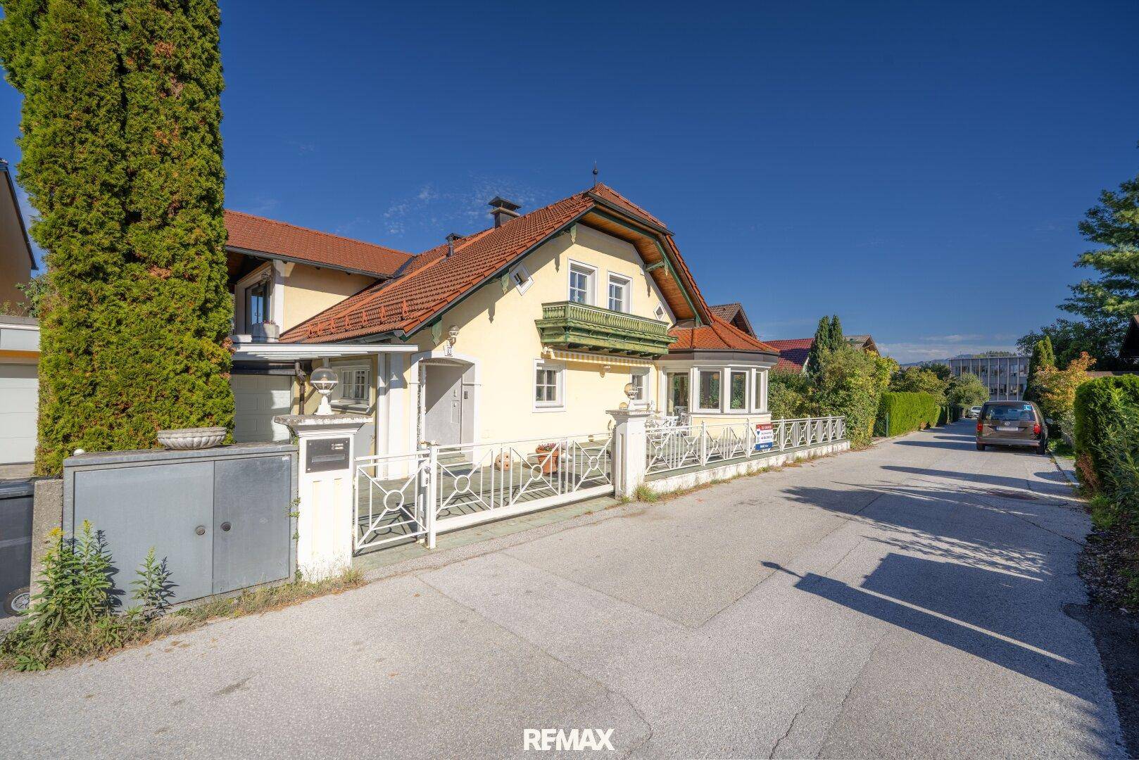 Ansicht des Hauses von der Straße mit gelber Fassade, weißem Zaun und gepflegter Hecke.
