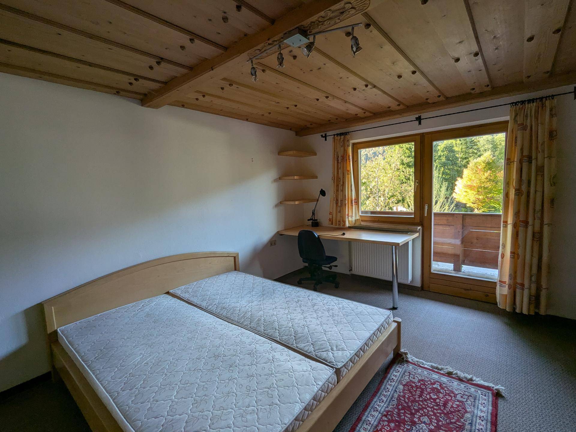 Schlafzimmer mit zwei Einzelbetten, Schreibtisch und Zugang zu einem Balkon mit Blick ins Grüne.