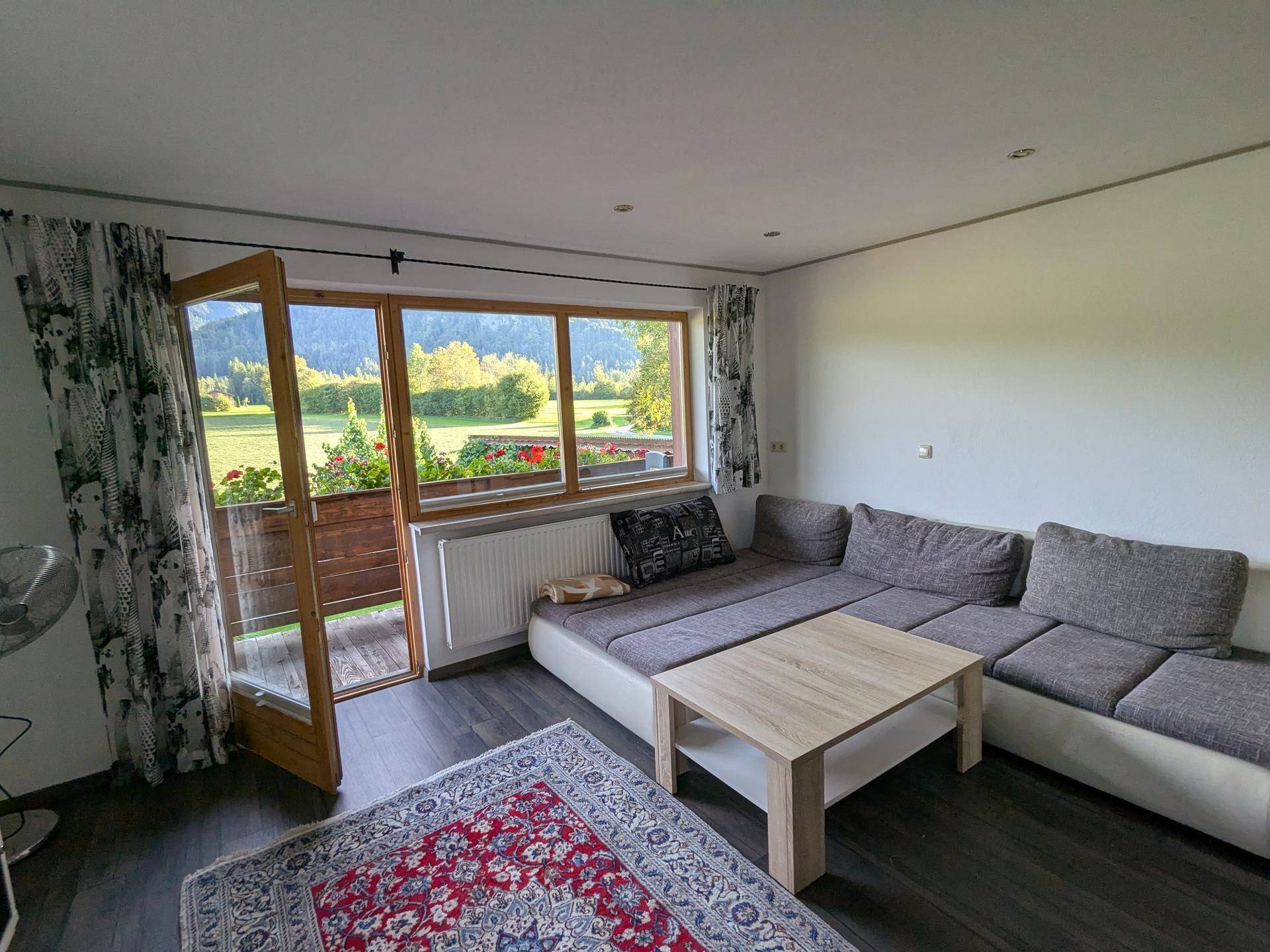Helles Wohnzimmer mit bequemer Couch, Couchtisch und Zugang zum Balkon mit Bergblick.