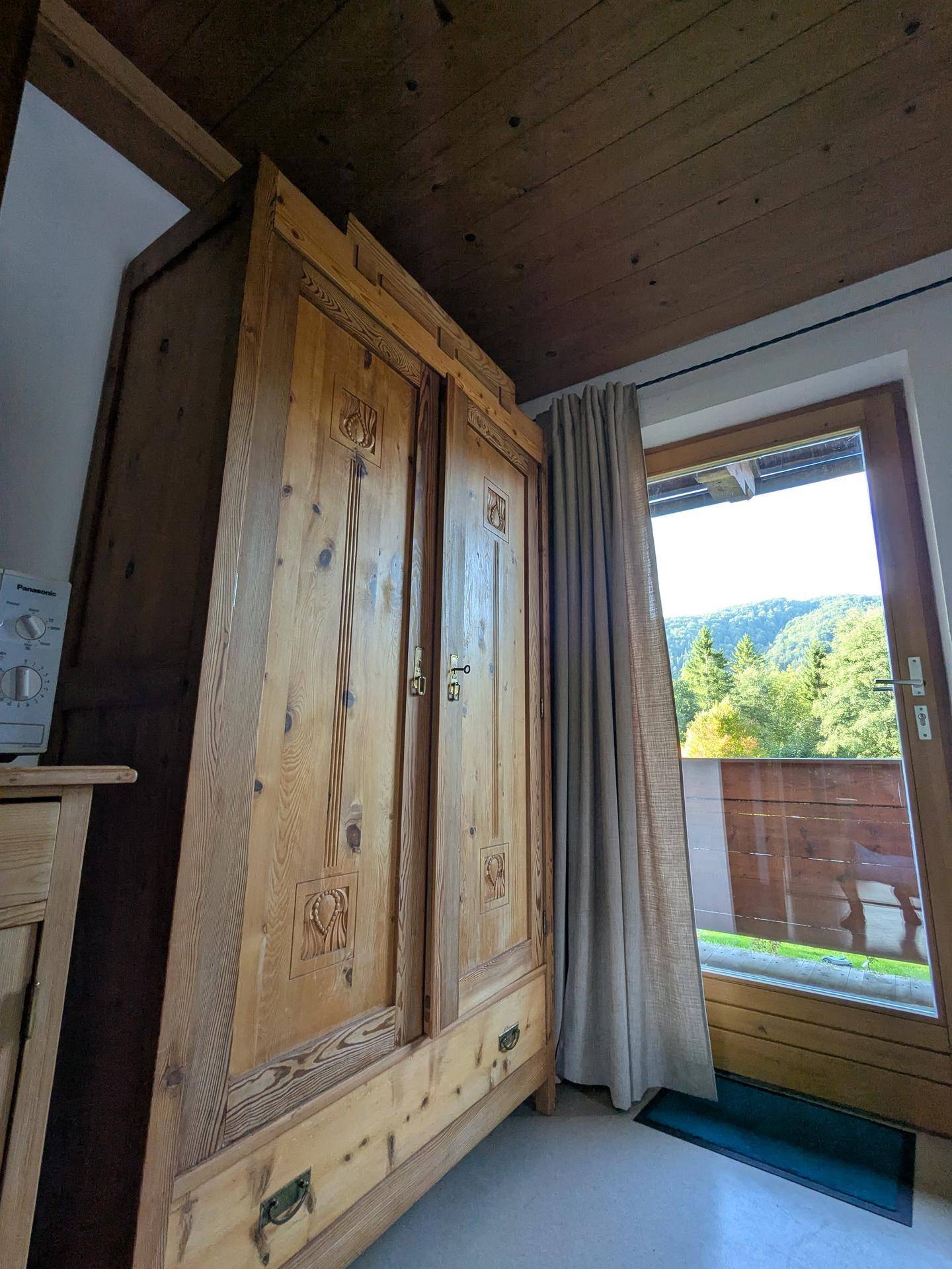 Schlafzimmer mit großem Holzschrank und Balkonzugang, umgeben von natürlicher Landschaft.