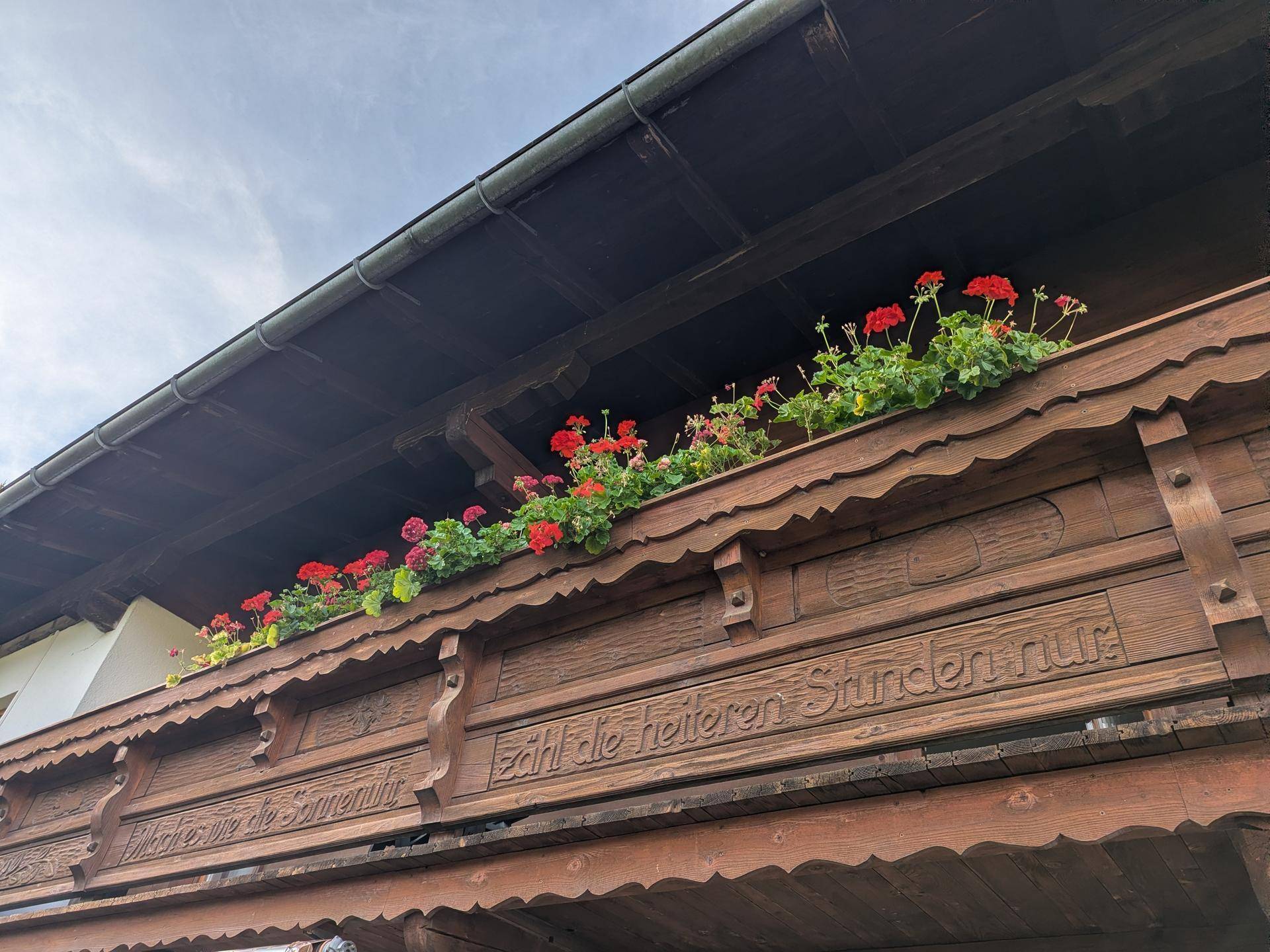 Traditioneller Holzbalkon mit kunstvollen Schnitzereien und farbenfrohen Blumenkästen.