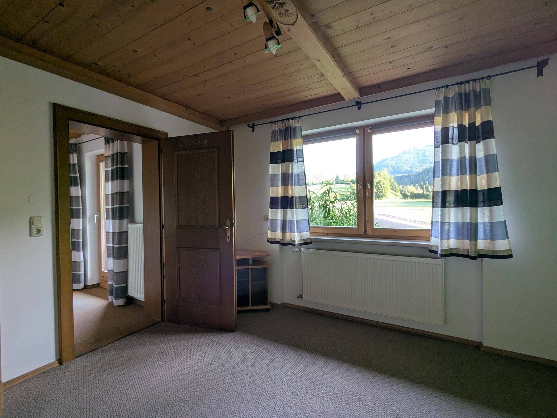 Geräumiges Zimmer mit Holzbalkendecke, Teppichboden und Fenster mit Bergblick.