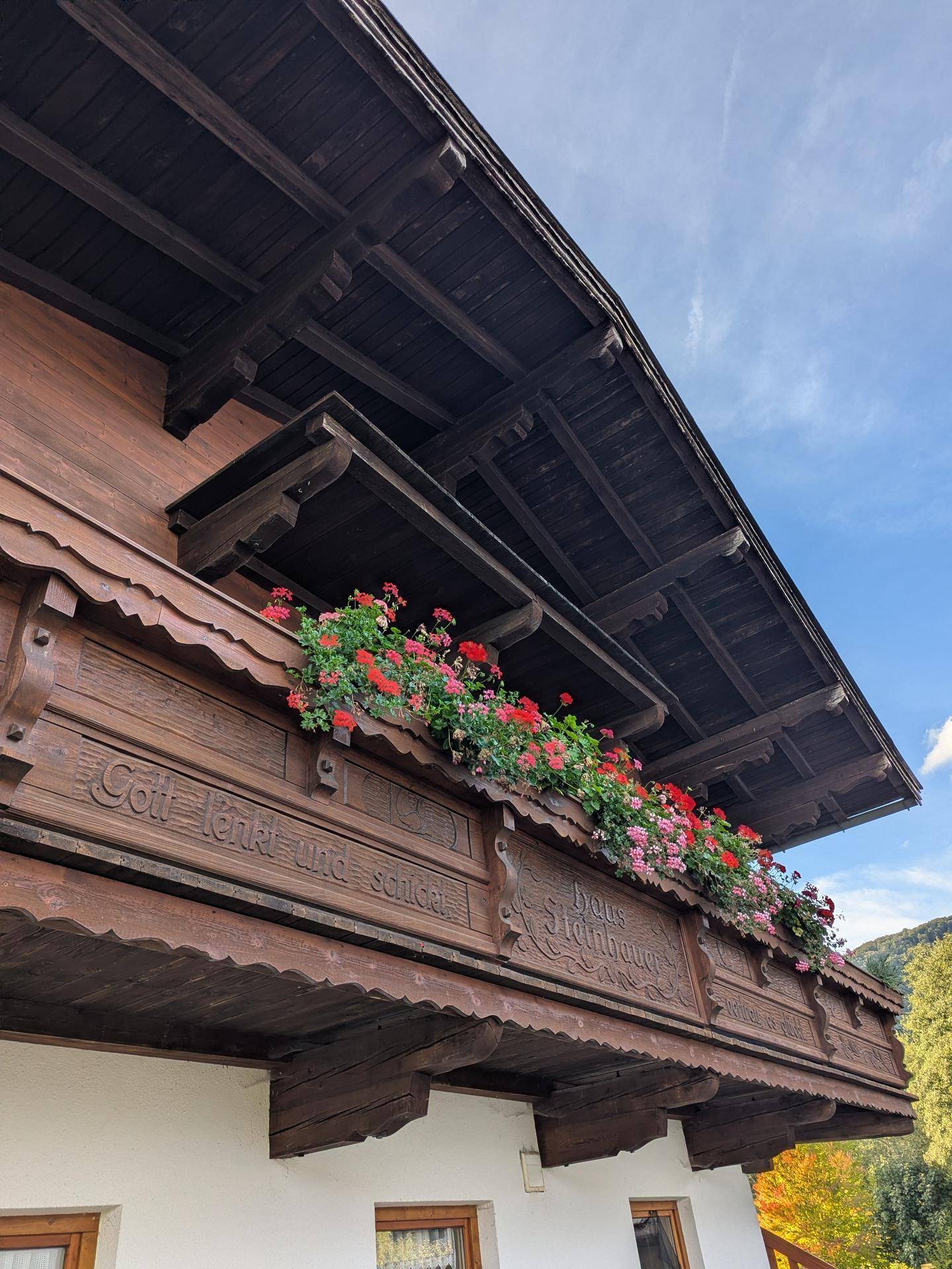 Detailansicht eines traditionellen Holzbalkons mit Schnitzereien und bunten Blumenkästen.