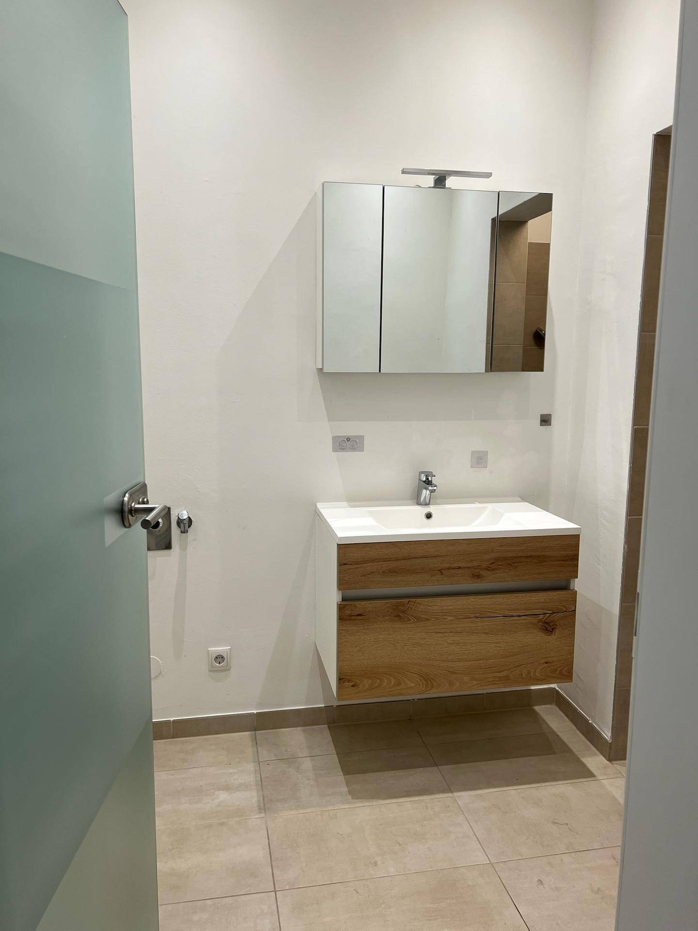 Modernes Badezimmer mit schwebendem Waschtisch, Spiegelschrank und hellen Fliesen.