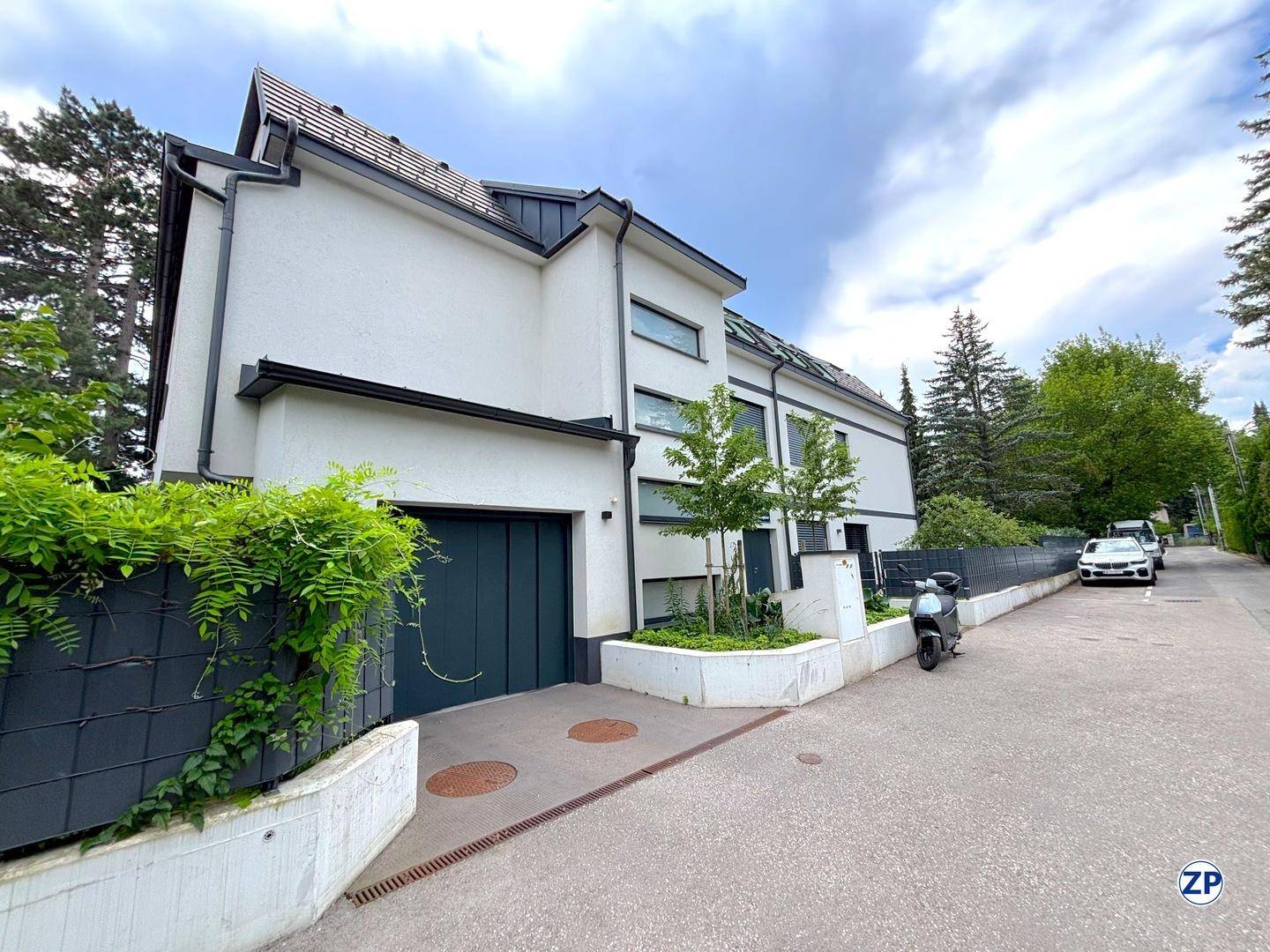 Modernes Mehrfamilienhaus mit weißer Fassade und dunklem Dach.