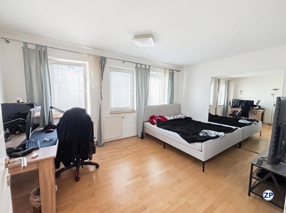 Geräumiges Schlafzimmer mit Doppelbett, Schreibtisch, Bürostuhl und zwei Fenstern mit Jalousien.