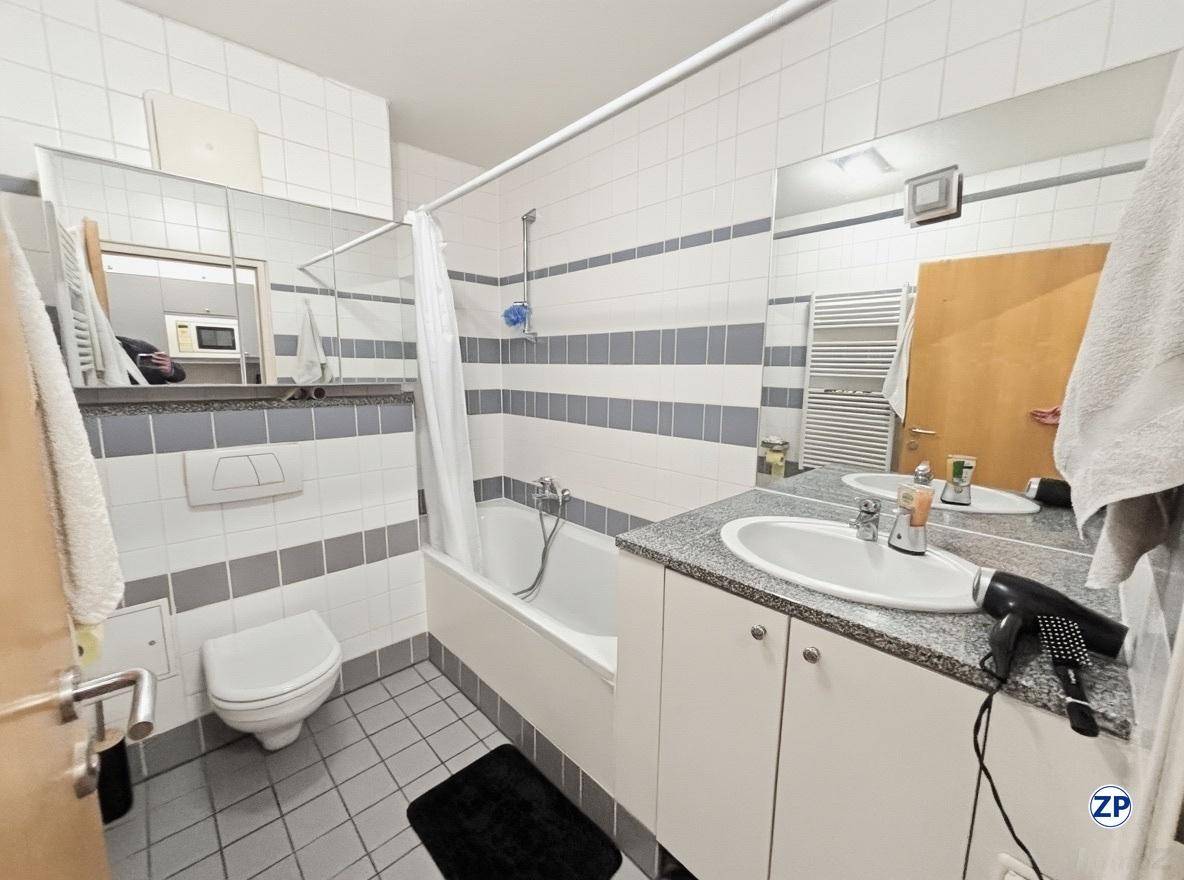 Badezimmer mit Badewanne, Toilette, Einzelwaschbecken und weiß-grau gefliesten Wänden und Boden.