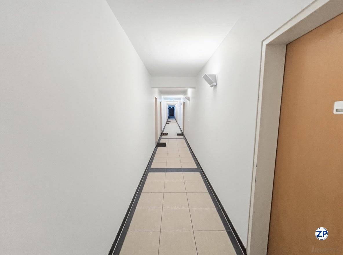 Langer, schmaler Flur mit hellen Fliesen und weißen Wänden, der zu mehreren Türen führt.