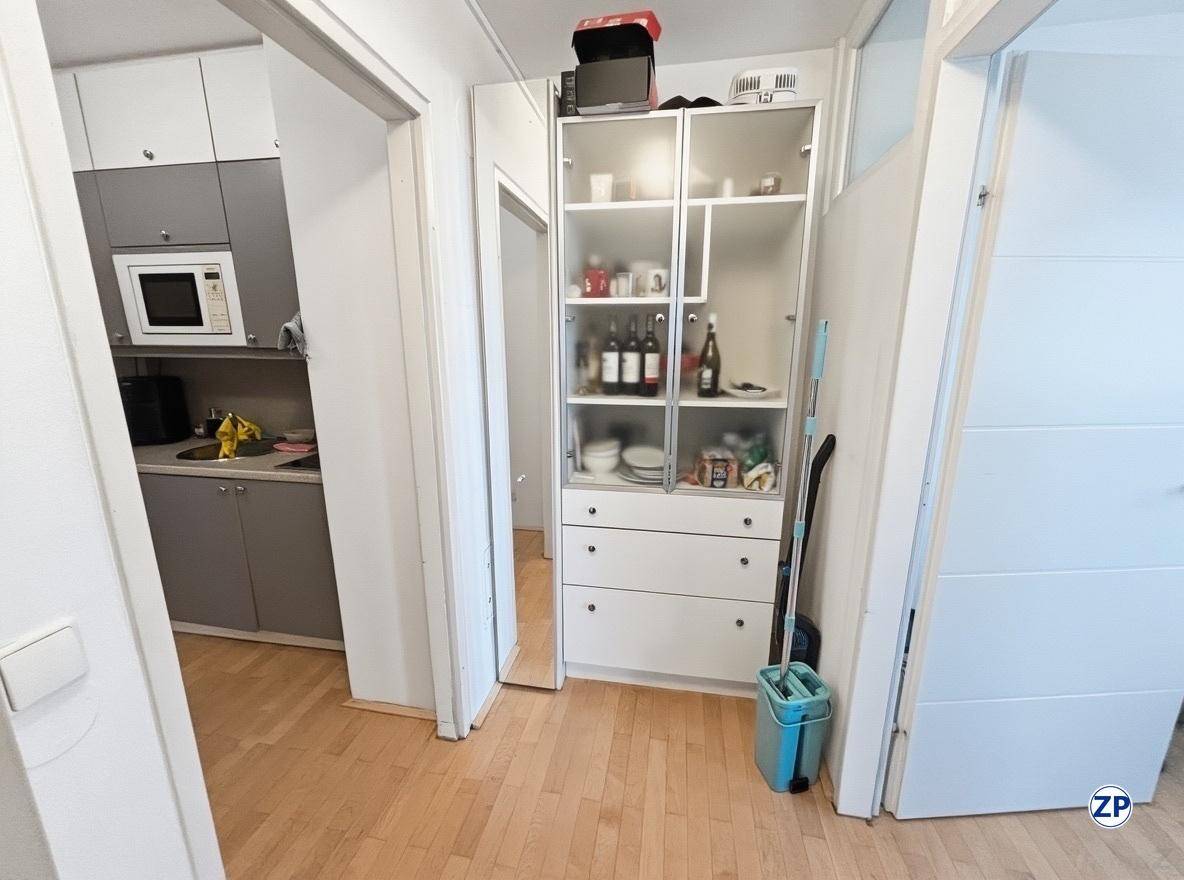 Flur mit weißem Vitrinenschrank, der zur angrenzenden Küchenzeile führt, mit Holzfußboden.