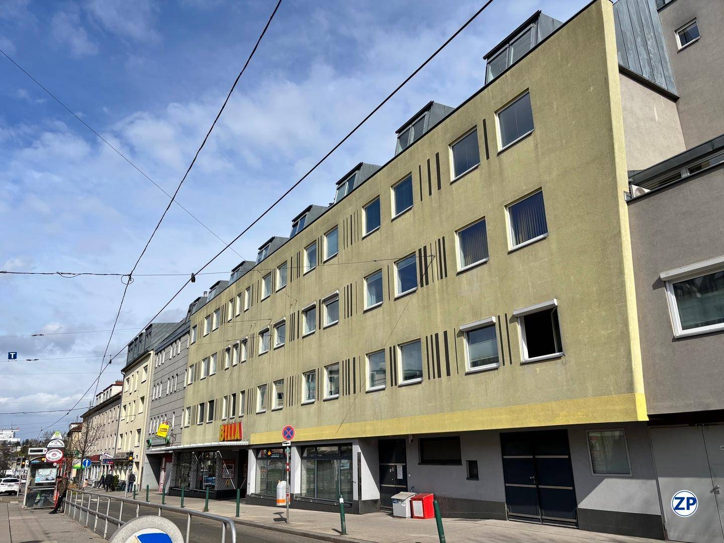 Außenansicht eines mehrstöckigen Gebäudes mit Geschäften im Erdgeschoss und Wohnungen darüber.