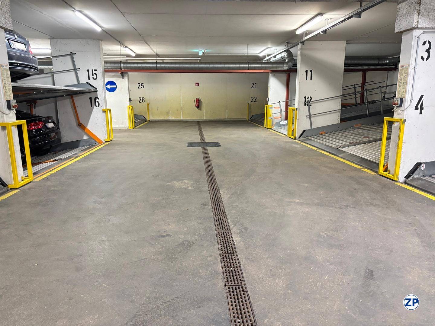 Tiefgarage mit Parkliftsystemen und Betonboden, gut beleuchtet und organisiert.