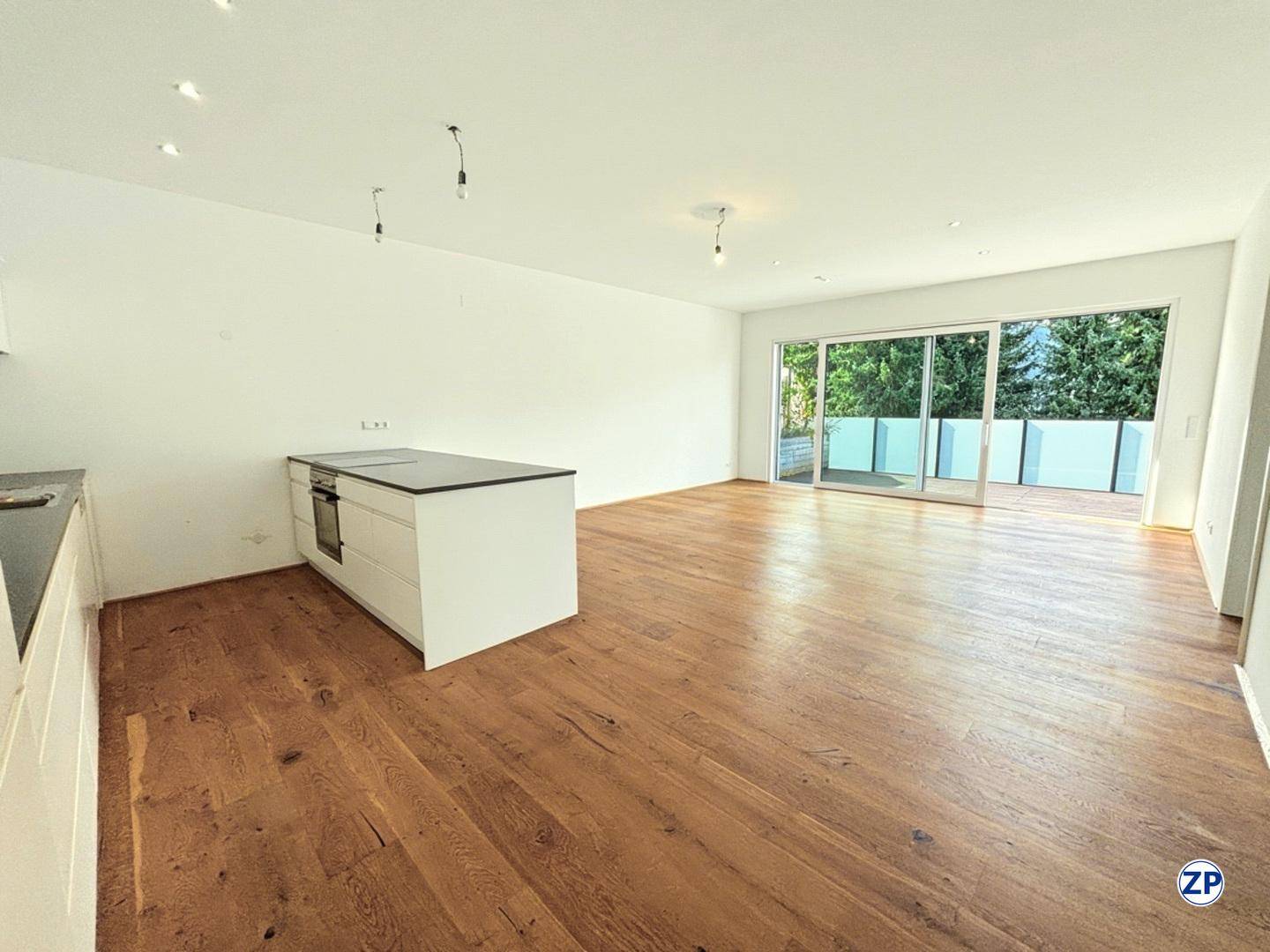 Heller offener Wohnbereich mit Holzboden, Kücheninsel und Zugang zu einem großen Balkon.
