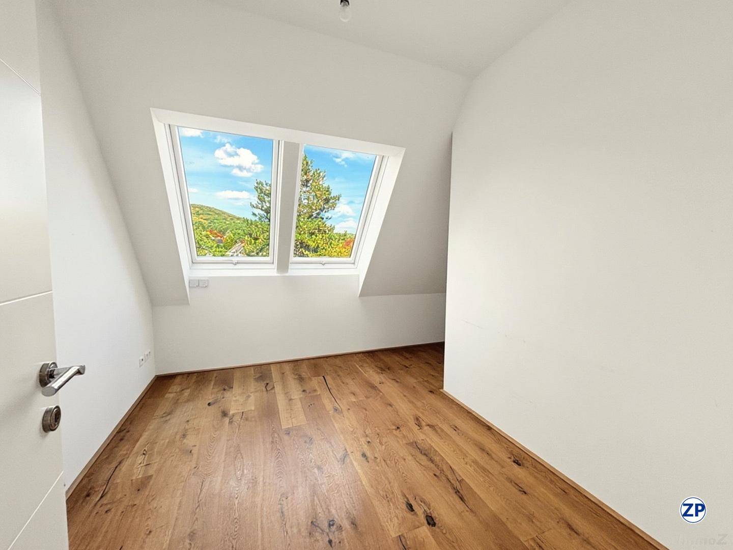 Dachgeschosszimmer mit Holzboden und großem Dachfenster, das viel Tageslicht hereinlässt.