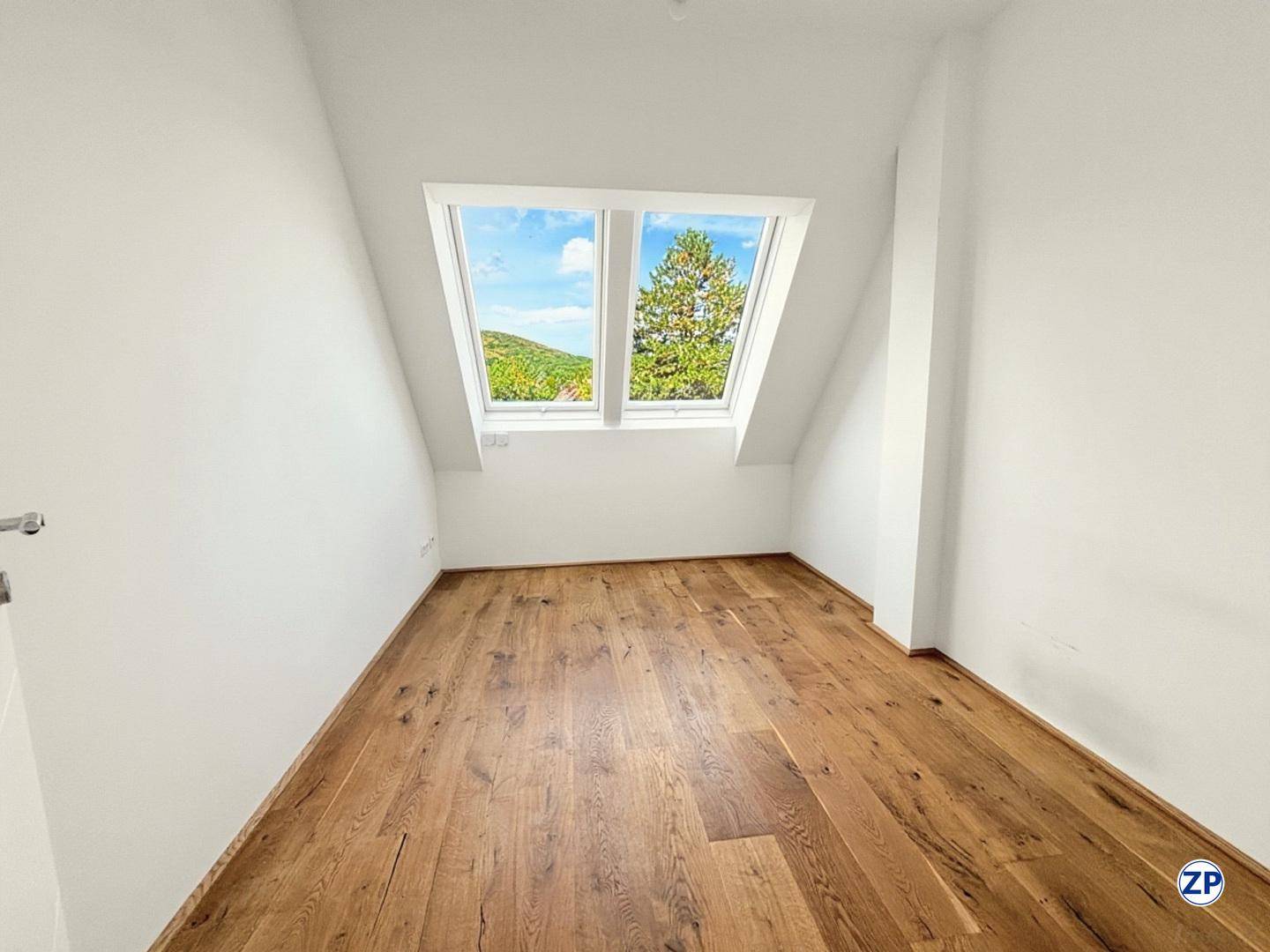 Geräumiges Zimmer im Dachgeschoss mit Holzboden und weitem Blick durch das Dachfenster.