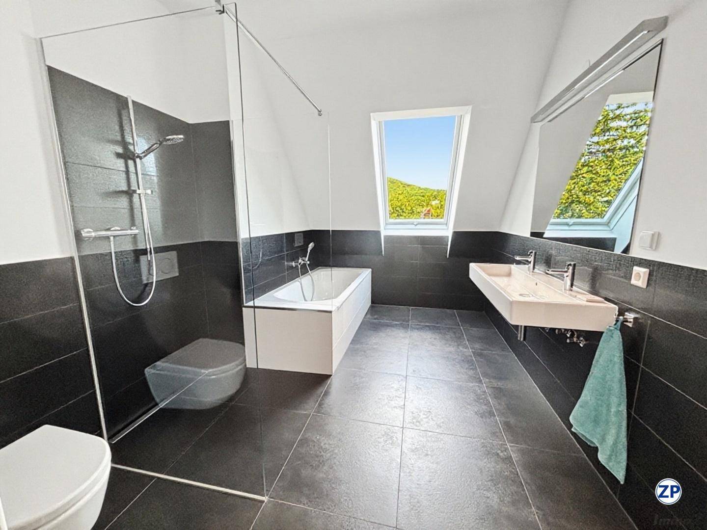 Modernes Badezimmer mit dunklen Fliesen, Badewanne, Dusche und Dachfenster.