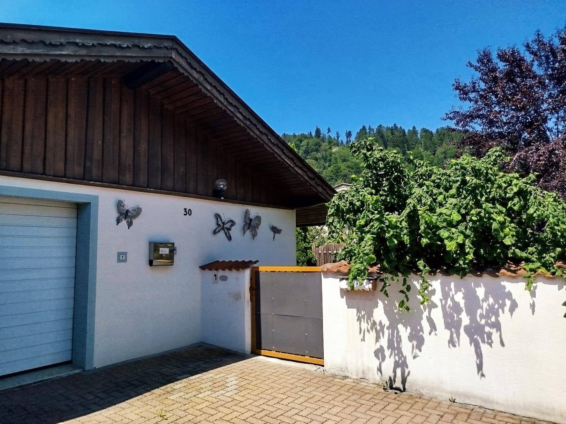 Seitenansicht des Hauses mit Eingangsbereich, gepflastertem Weg und üppiger grüner Bepflanzung.
