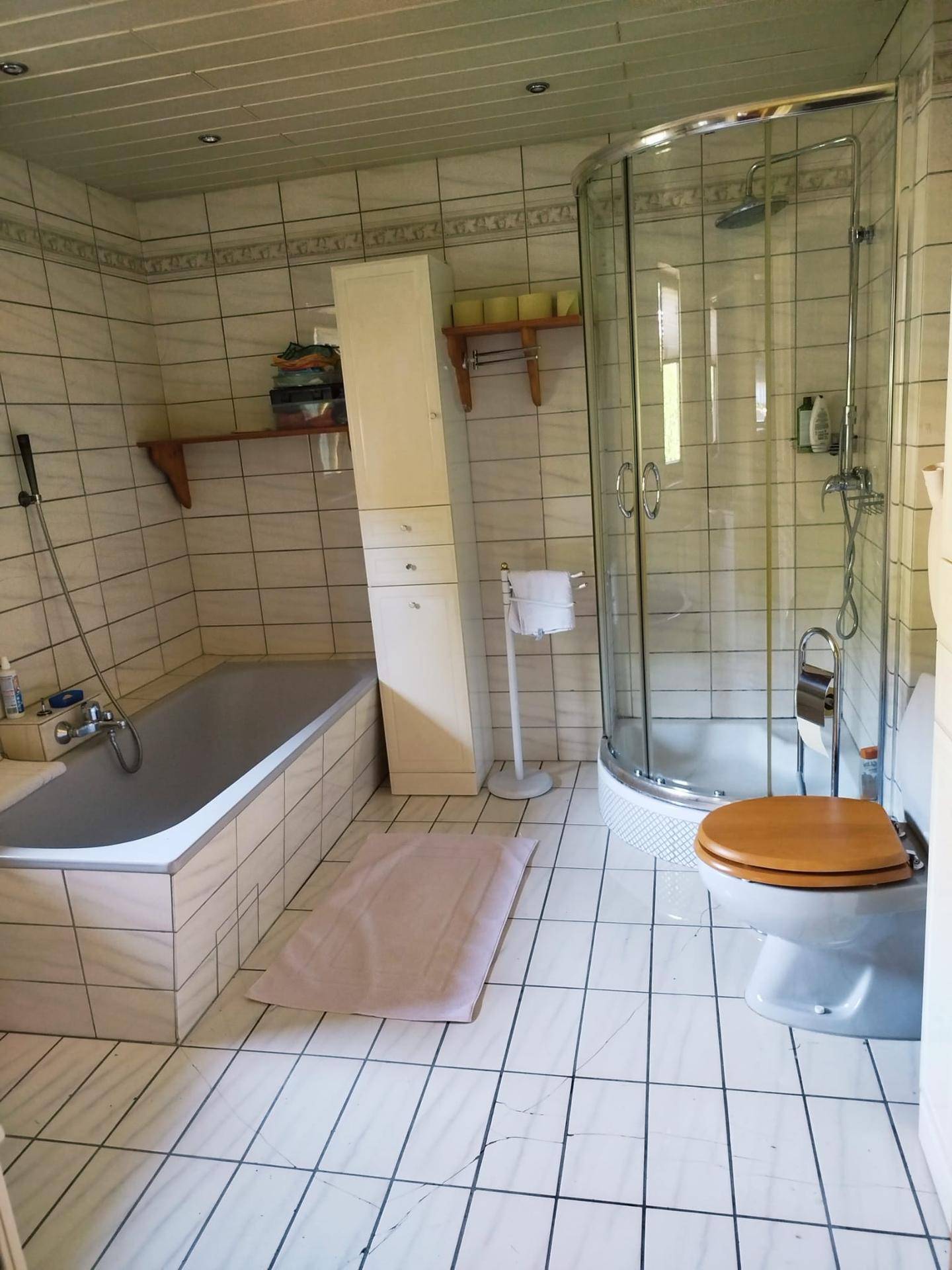 Helles Badezimmer mit Badewanne, Duschkabine, WC und weißen Fliesen an Wänden und Boden.